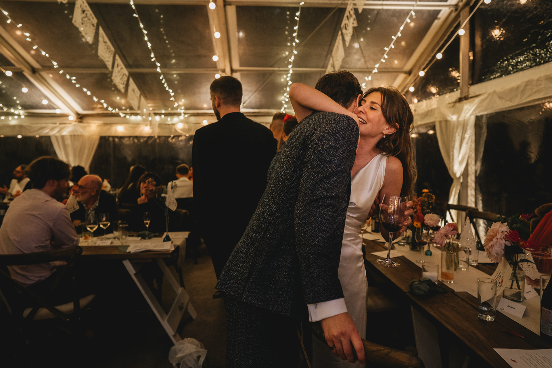 A bride hugging her groom in a marquee lit with fairy lights