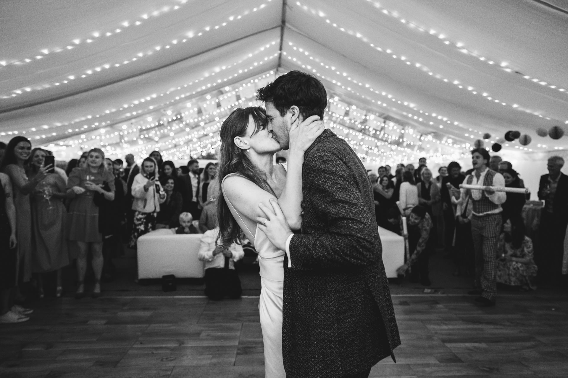 Bride and groom kissing during their first dance with wedding guests watching in a marquee