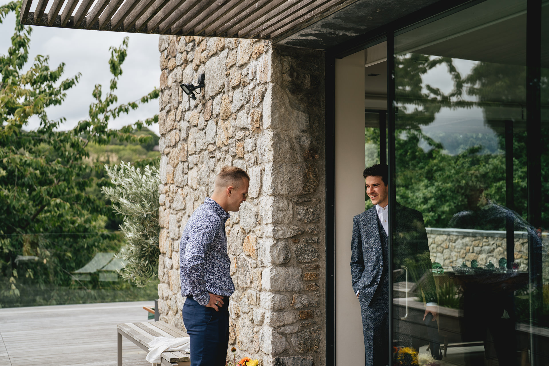 A groom to be talking with a groomsman at a beautifully designed house with Dartmoor views reflected in the window