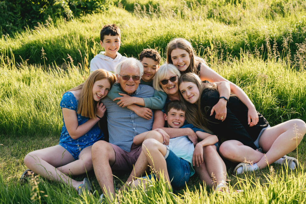 A group of grandchildren cuddling together with their grandparents, sitting on some grass