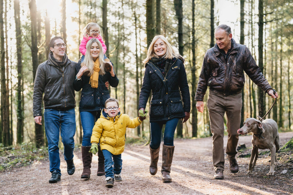 An extended family group walking together through sunny woodland during a photography session in Devon