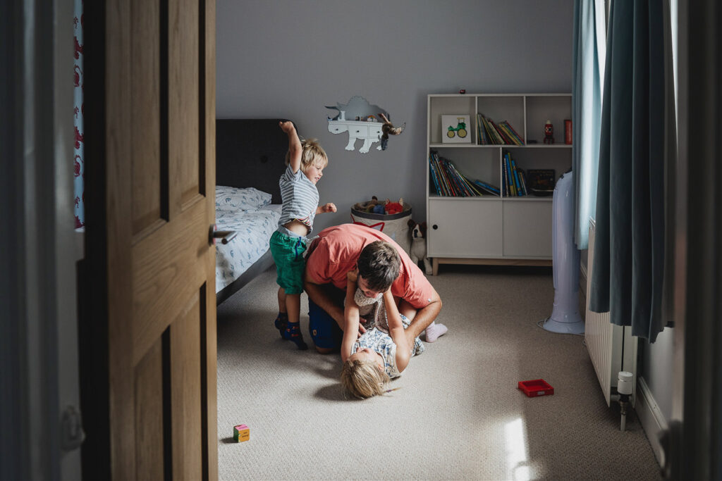 A family photography session at home in Devon with a father playing in a bedroom with two children