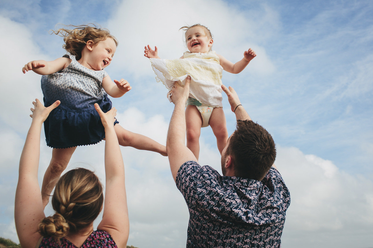 Two young girls laughing while their parents throw them up into the air for a family photo at the beach