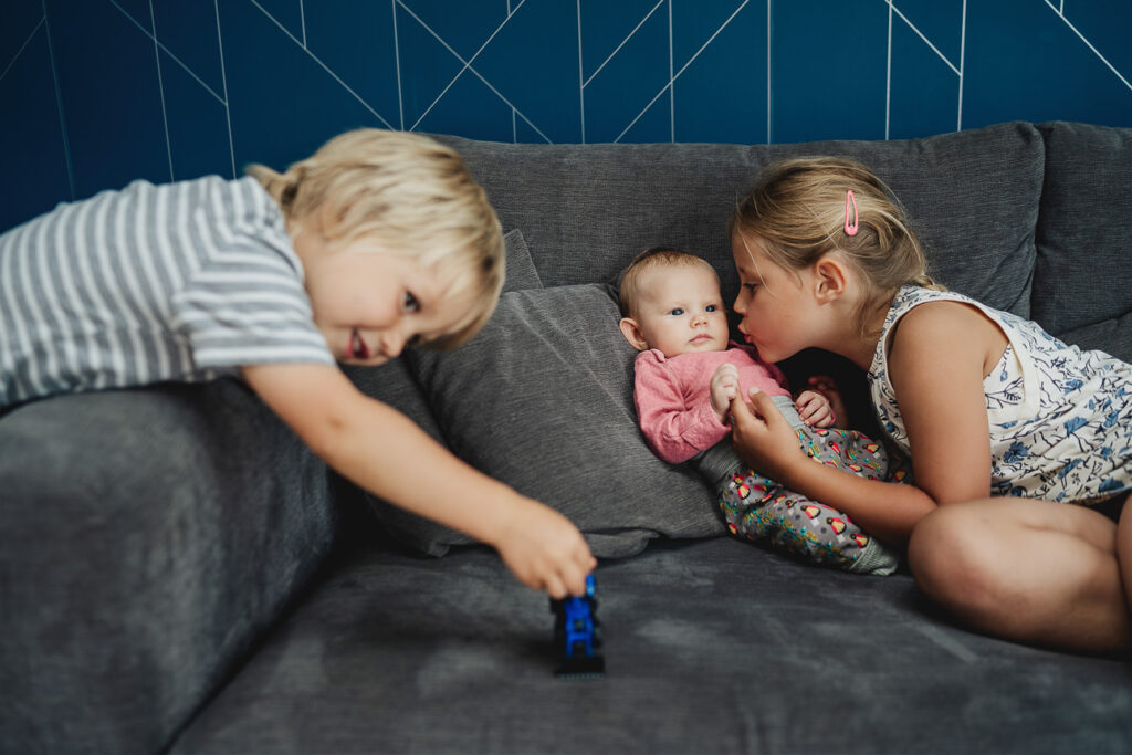 Three young siblings on a grey sofa during a family photography session at home in Devon