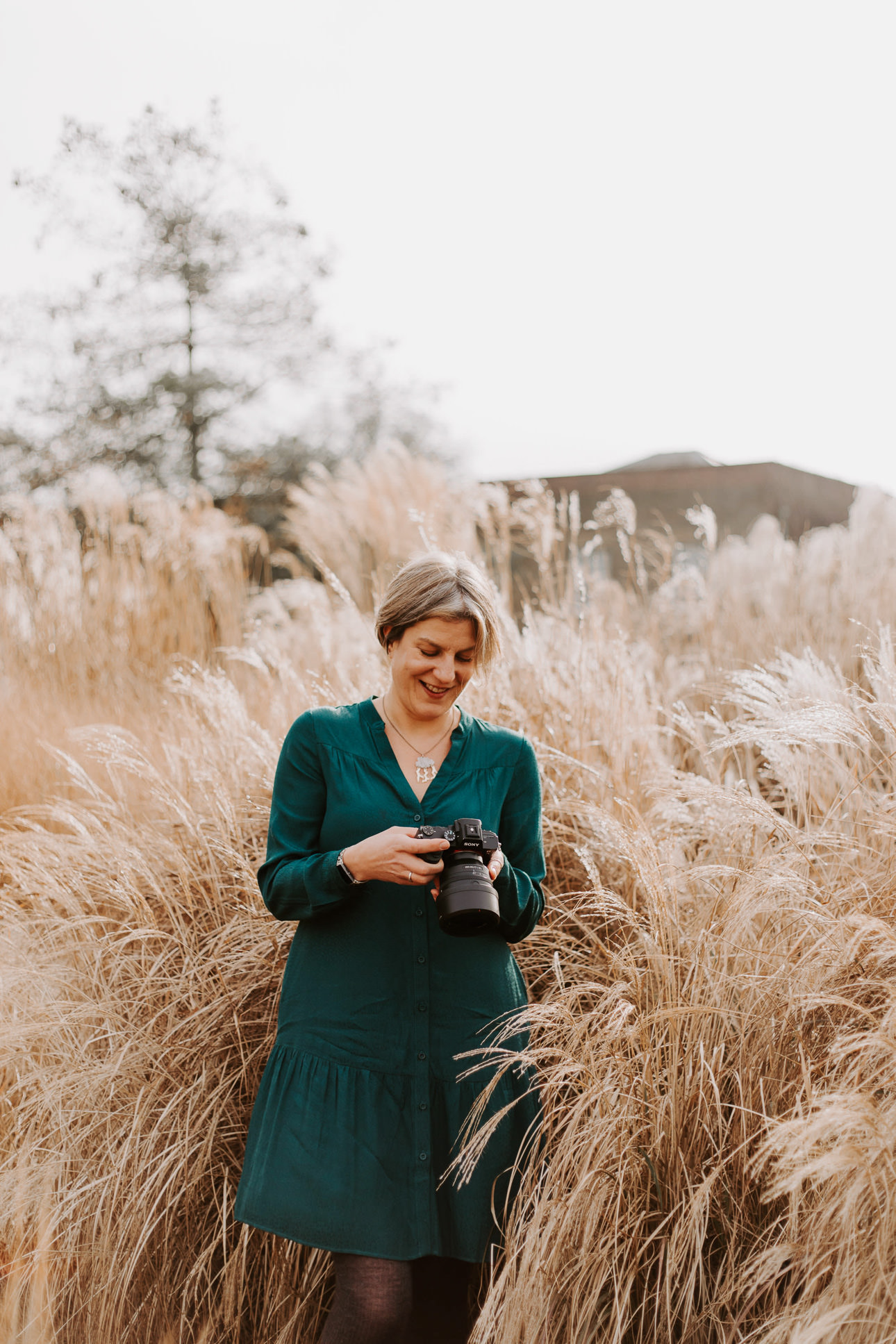 Photographer Helen Lisk wearing a green dress in a grassy field and looking down at her camera