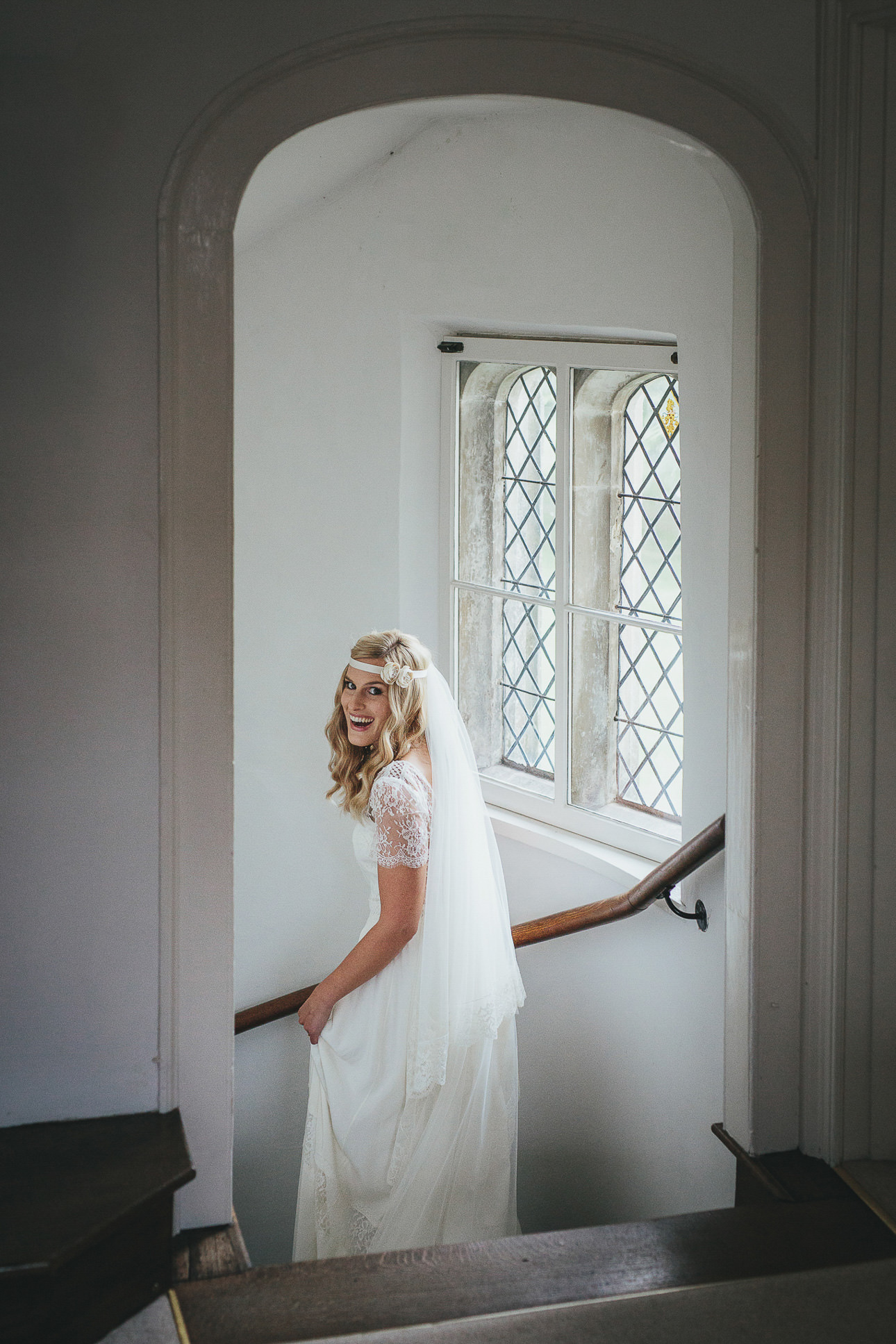 A bride looking back and smiling as she walks down a stairwell at Cadhay in Devon