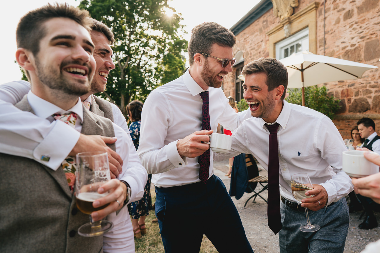 A relaxed group of wedding guests all laughing with drinks in evening sunlight at a Somerset wedding