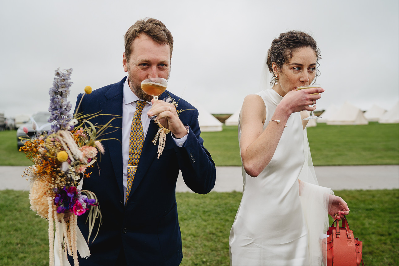 A stylish bride and groom sipping cocktails in a field