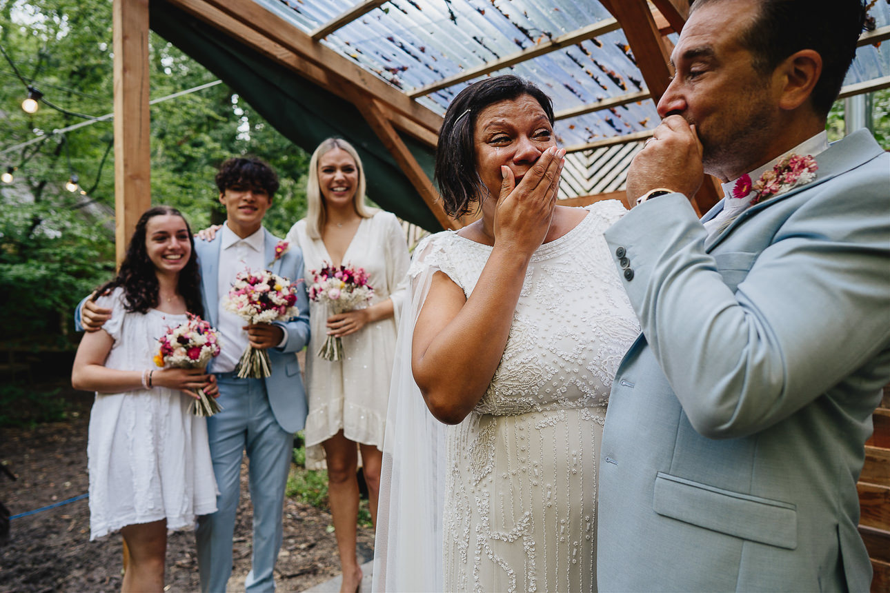 A bride and groom looking at each other and crying with family watching and smiling during an elopement wedding ceremony