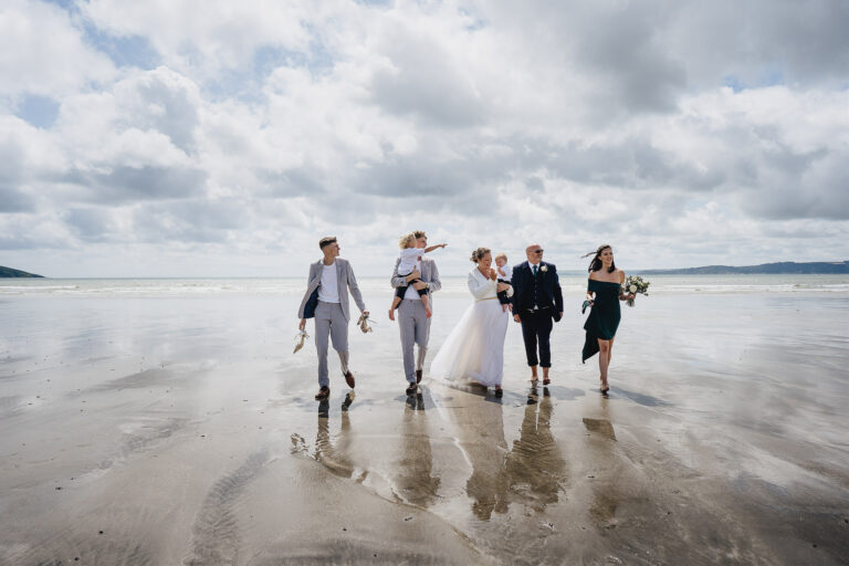 A family wedding group walking across the sand together on a beach in Cornwall at a small wedding celebration