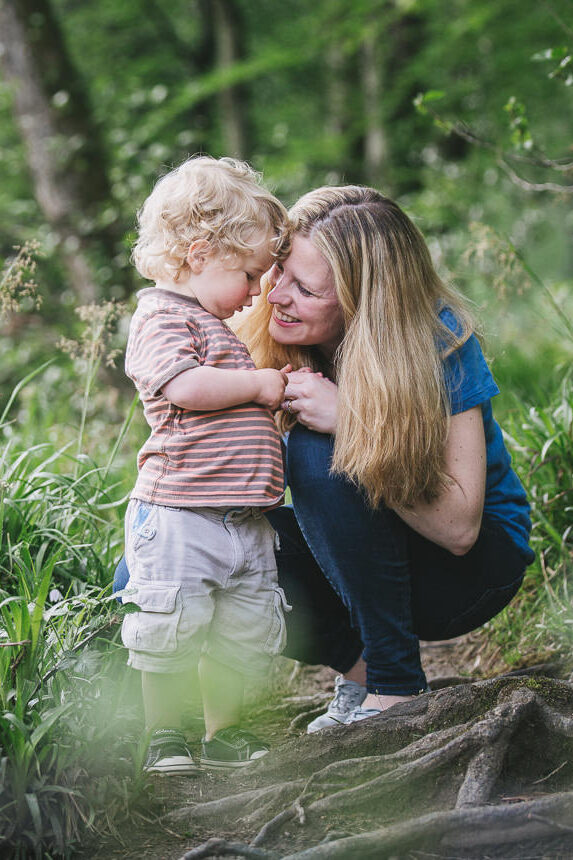 A mother with her young son squatting down amongst bluebells in the woodland during a family photography session