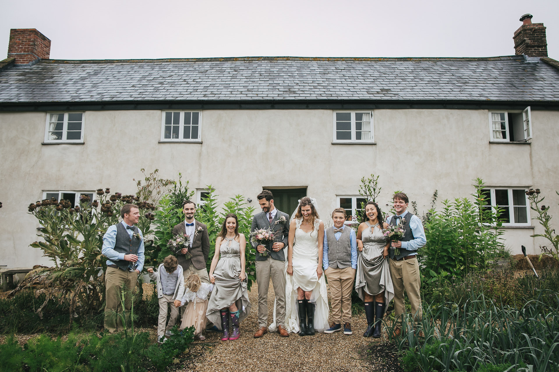 A relaxed wedding group photo with bride and groom in wellies outside River Cottage farmhouse at a River Cottage wedding