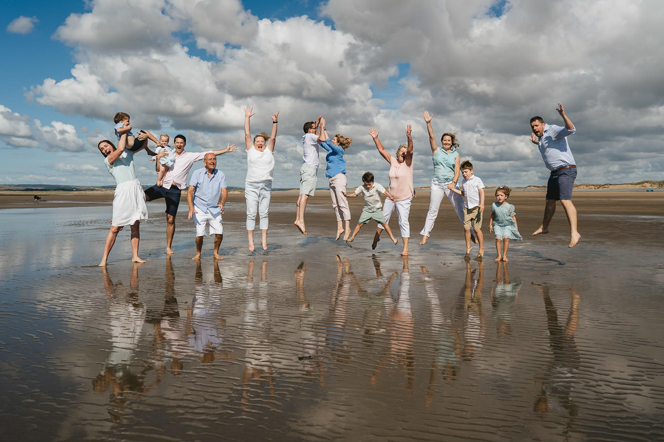 An extended family group photo on the beach in Devon, with everyone leaping in the air on the sand
