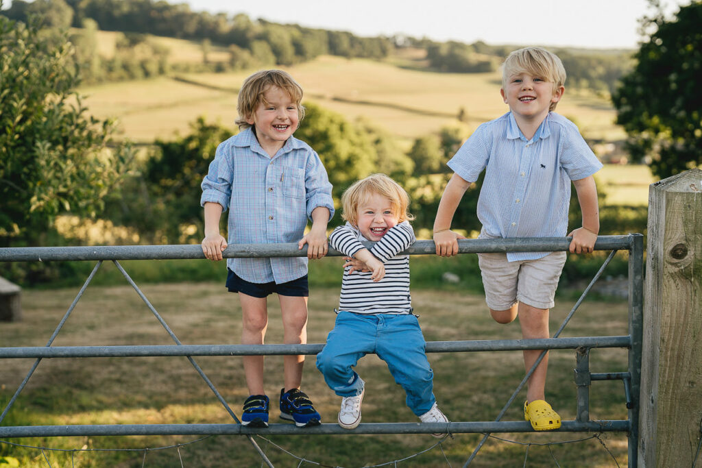 Three young cousins climbing on a gate together and laughing