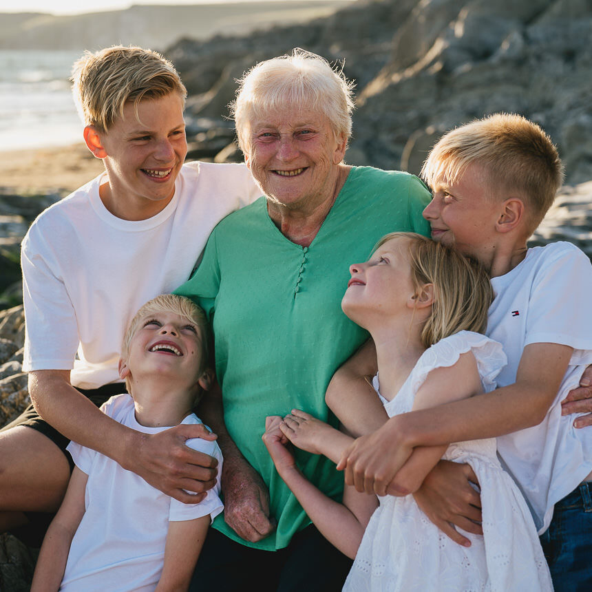 A grandmother with four grandchildren cuddling around her for a group photo on a beach in Devon