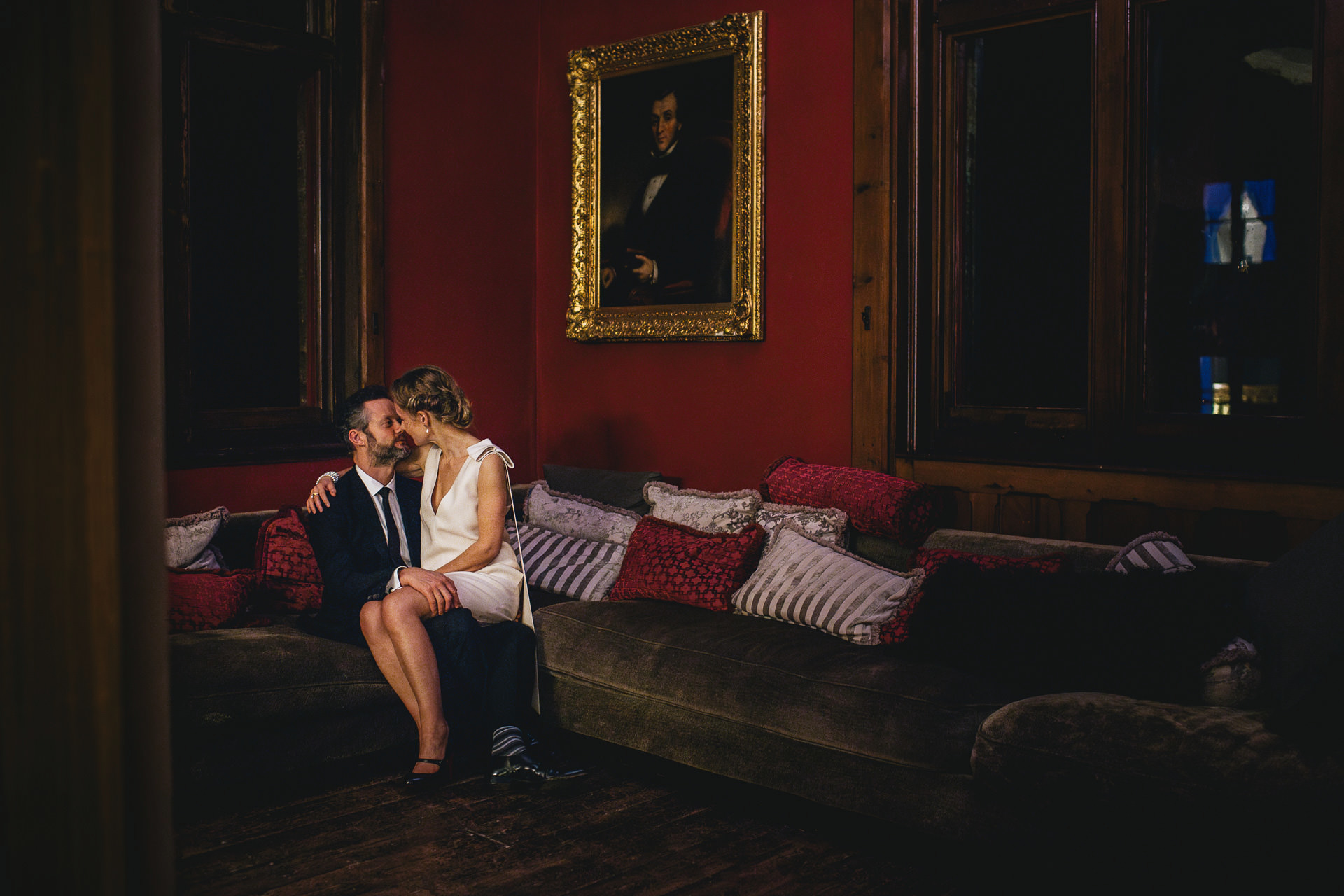 A stylish bride and groom sitting together on a sofa at night, at Huntsham Court in Devon
