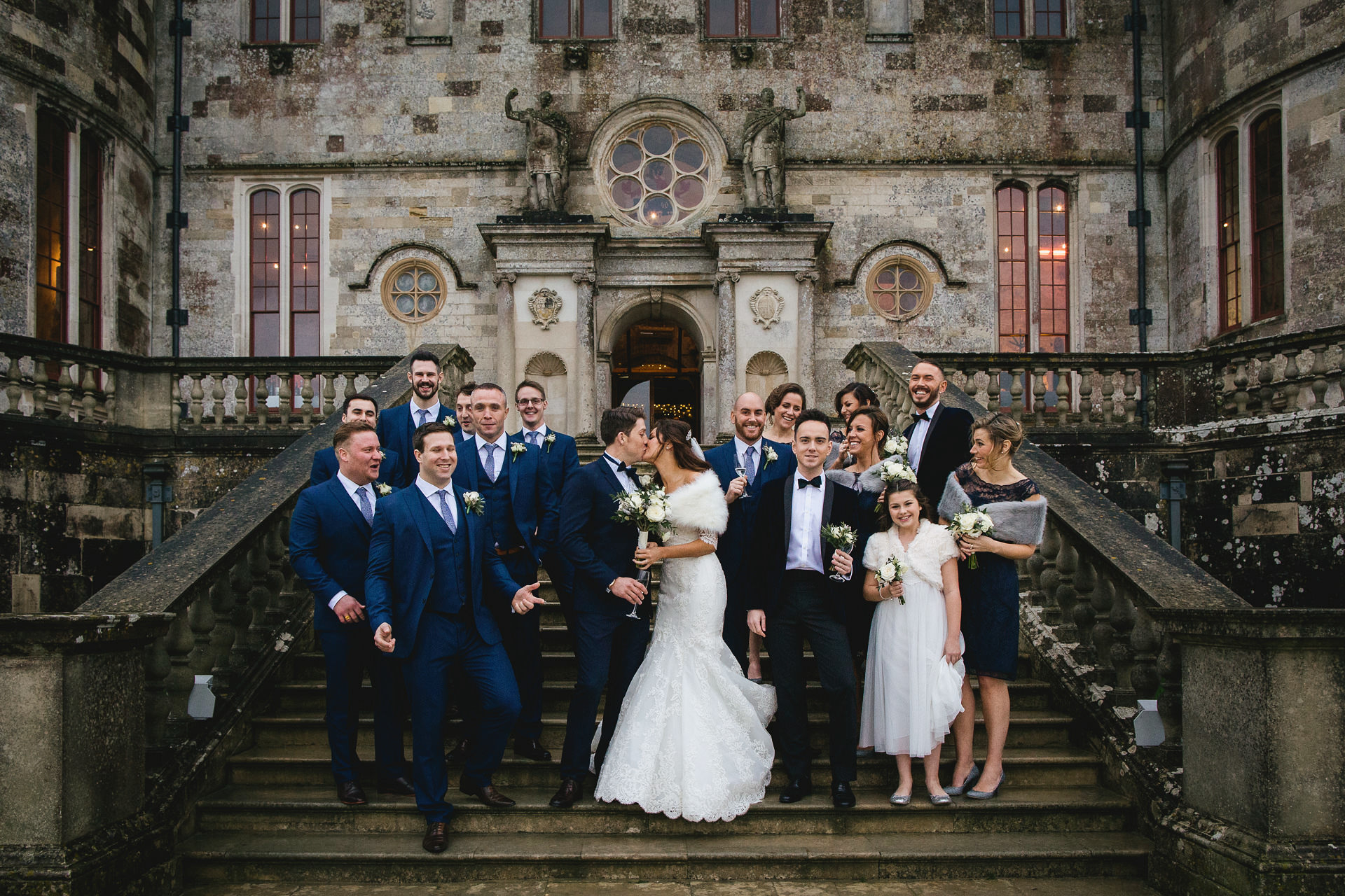 A relaxed group photo during a winter wedding at Lulworth Castle. Bride and groom standing with the wedding party on the castle steps. 
