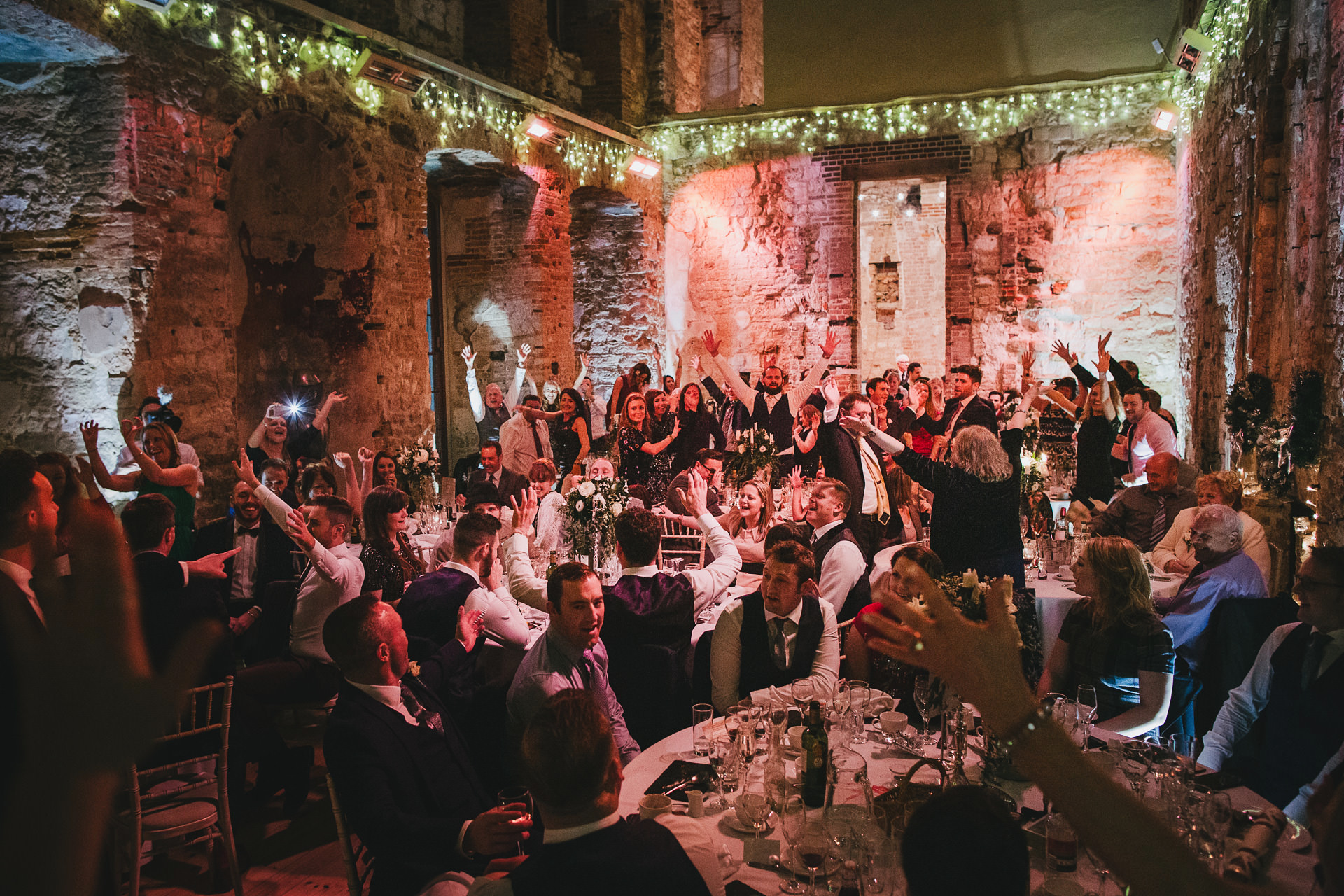 A winter wedding at Lulworth Castle, with a room full of wedding guests singing Christmas Carols at their tables