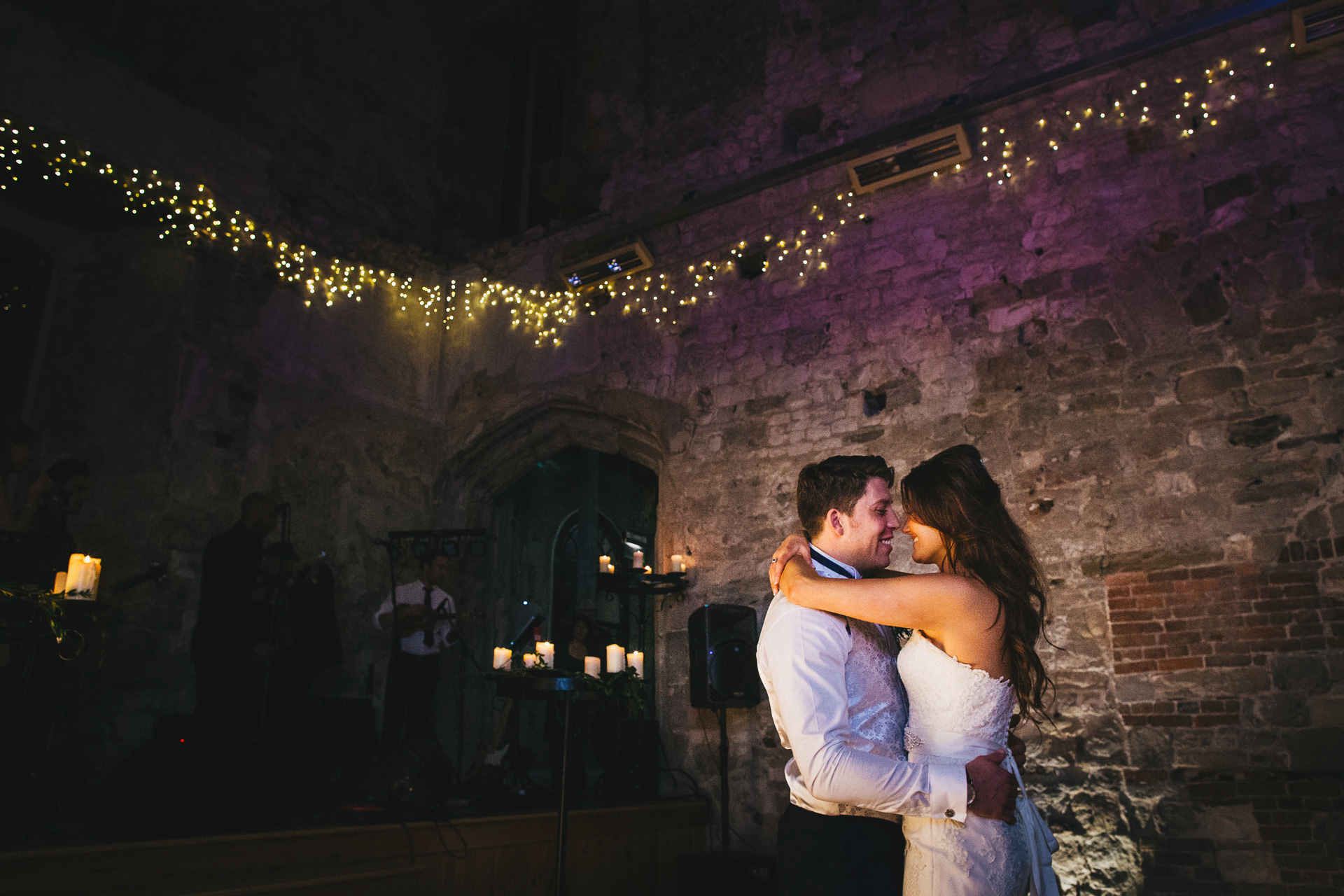 Lulworth Castle wedding with a bride and groom having their first dance with twinkling lights behind them