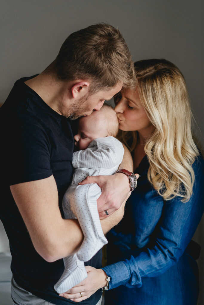 Two parents cuddling with a baby and kissing the baby's head
