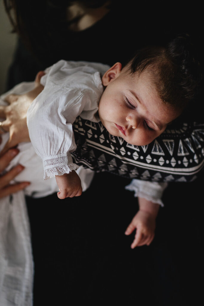 A sleeping baby in a white dress lying in a parent's arms