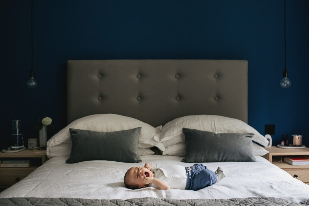 A newborn baby lying on a double bed with a blue bedroom wall