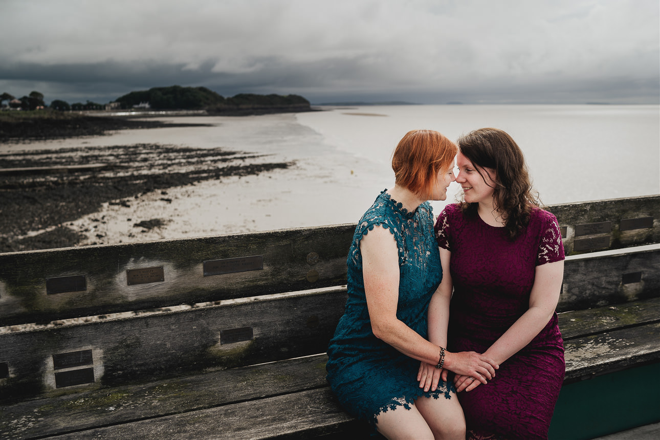 Two brides sitting together with a dramatic stormy sky behind them