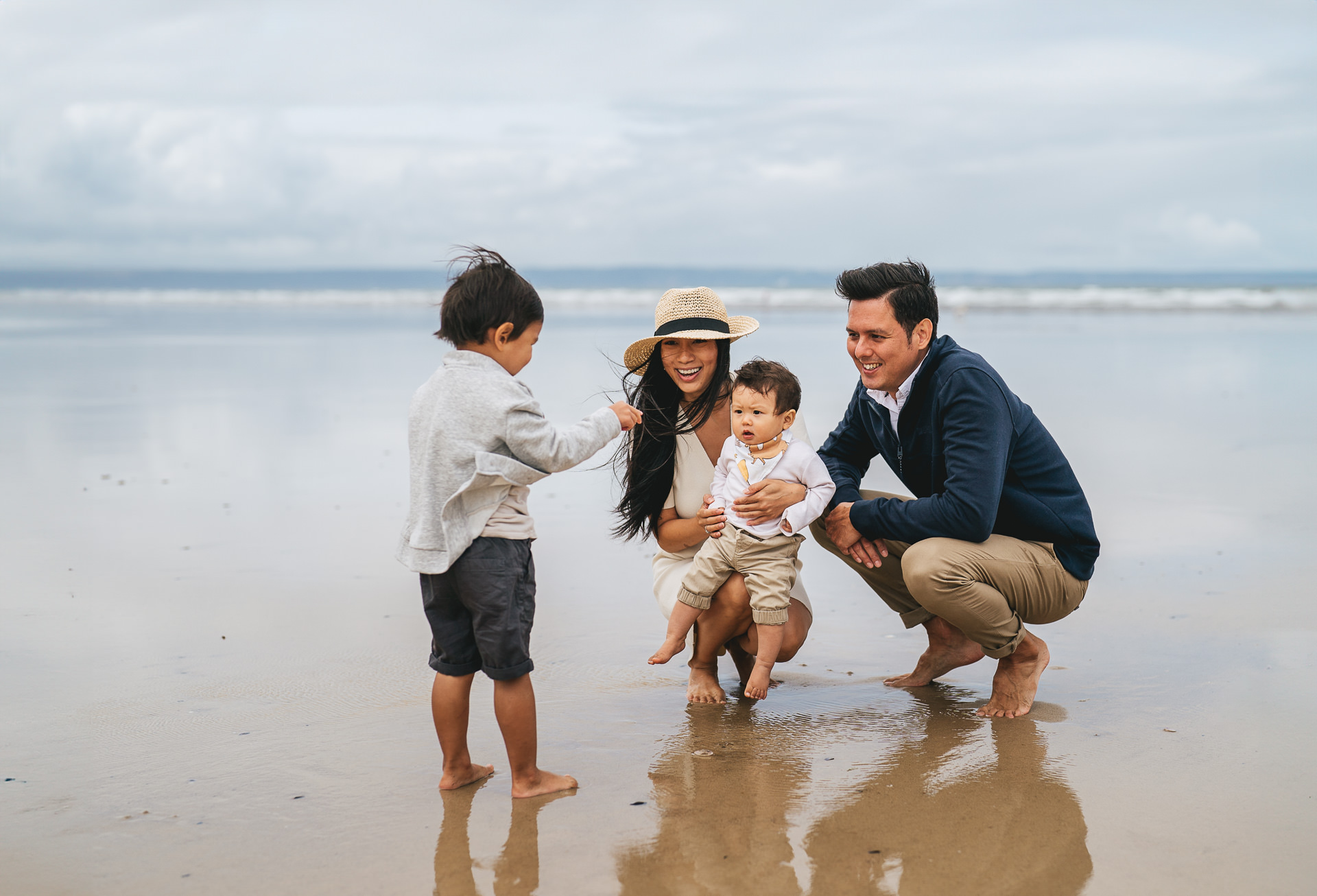 A family squatting down on the sand on the beach in North Devon, and smiling as they look at something together