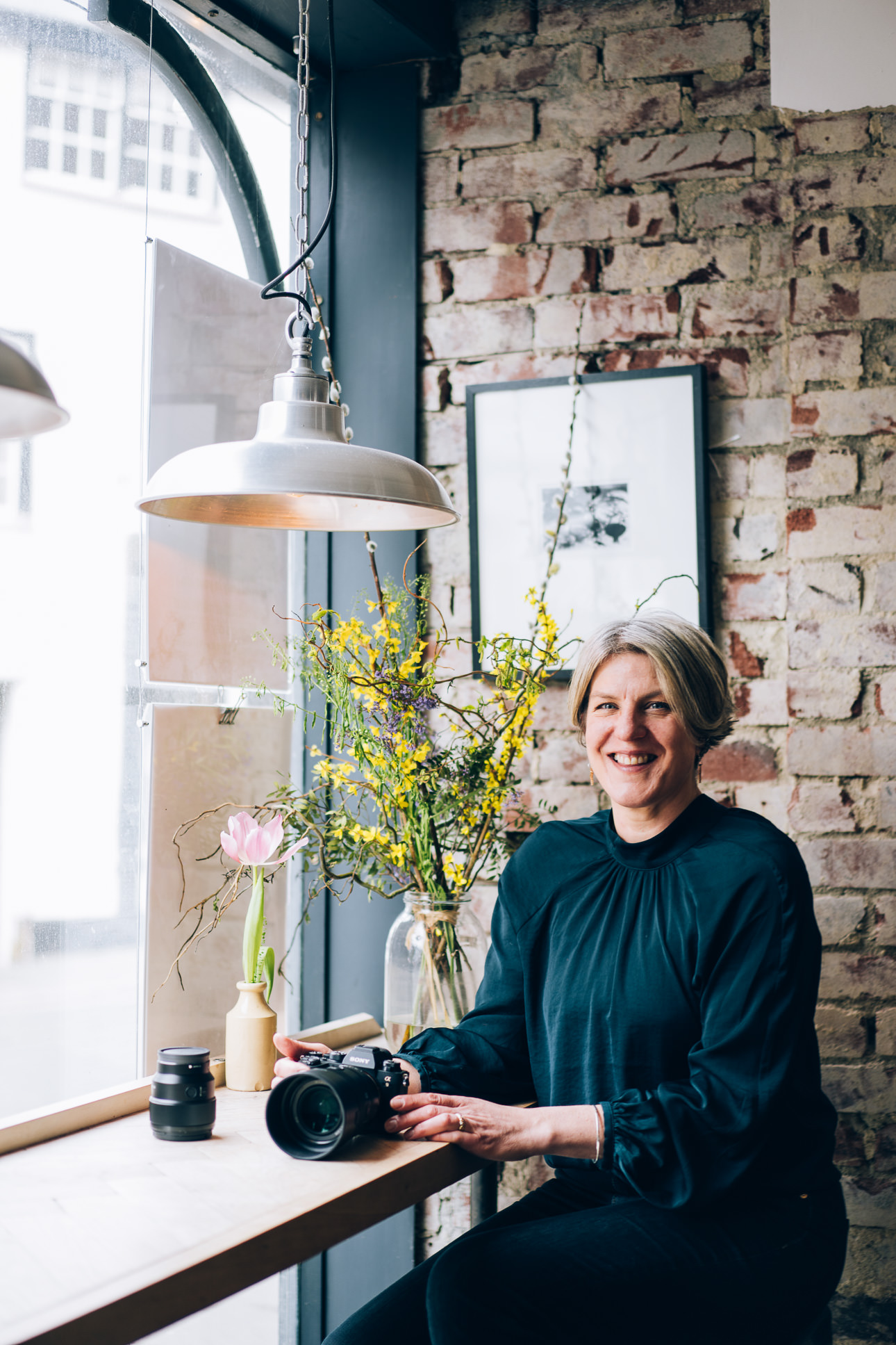 Devon photographer Helen Lisk sitting at a cafe table, smiling with a coffee and a camera