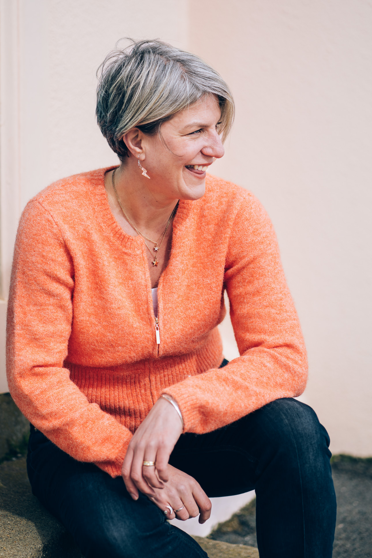 Devon photographer Helen Lisk in an orange cardigan, sitting on a step and laughing