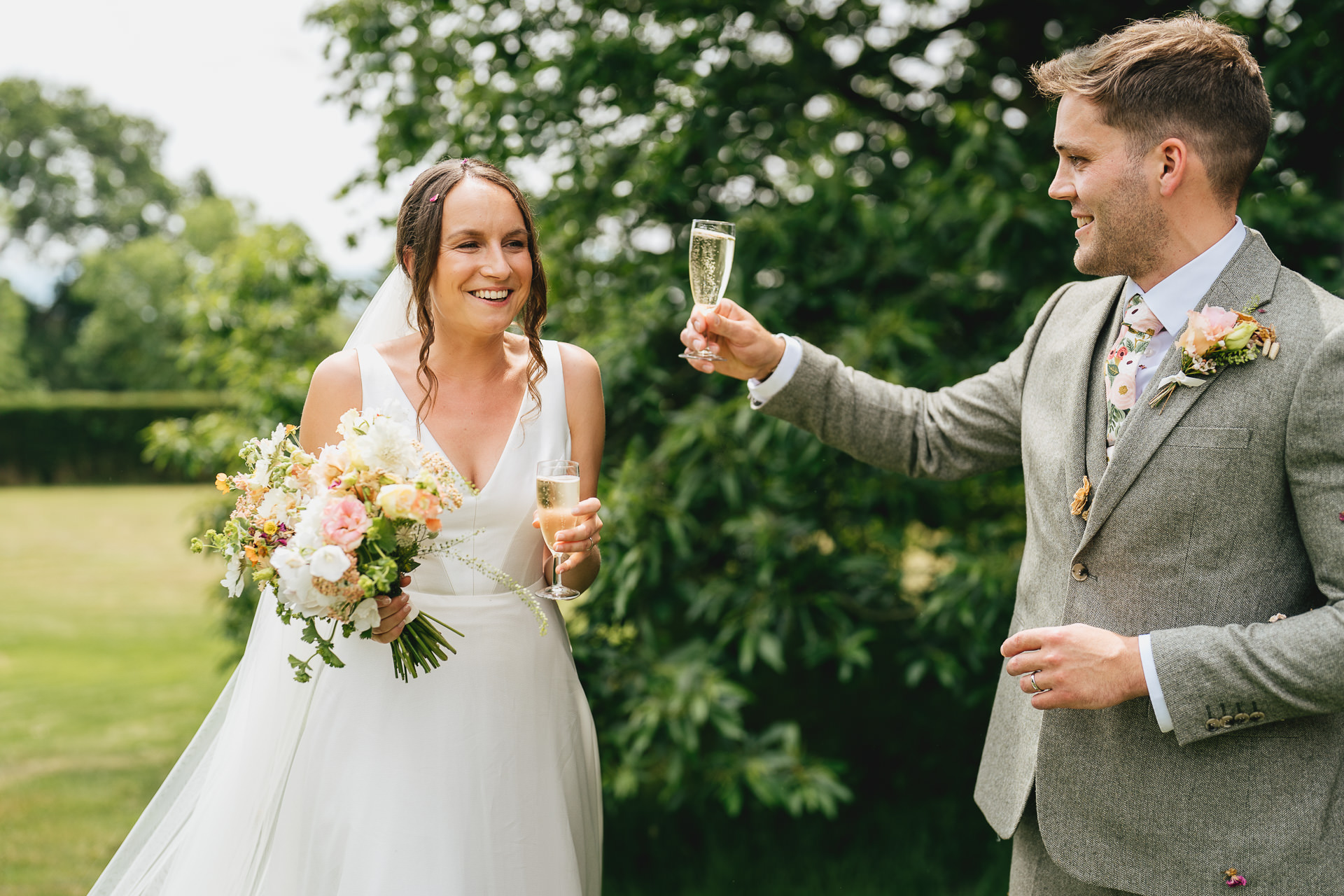A bride and groom raising glasses to each other in a garden setting