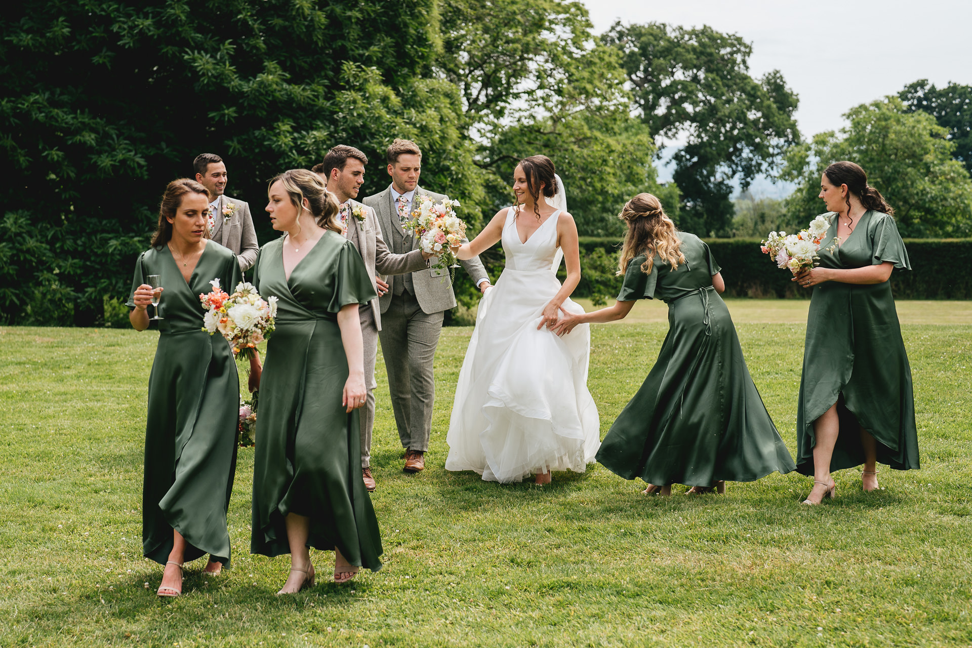 A bride and groom walking across a grass lawn with their wedding party