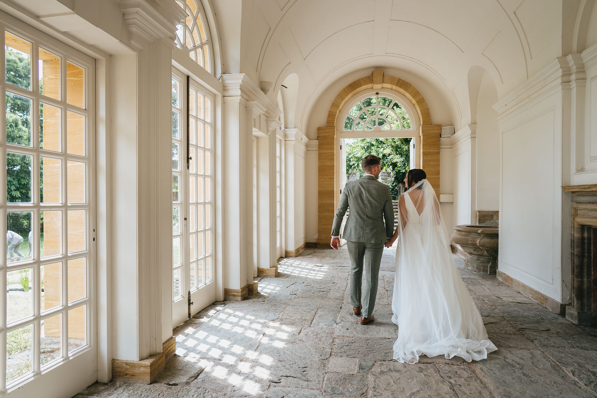 A bride and groom walking together through the orangery at Hestercombe