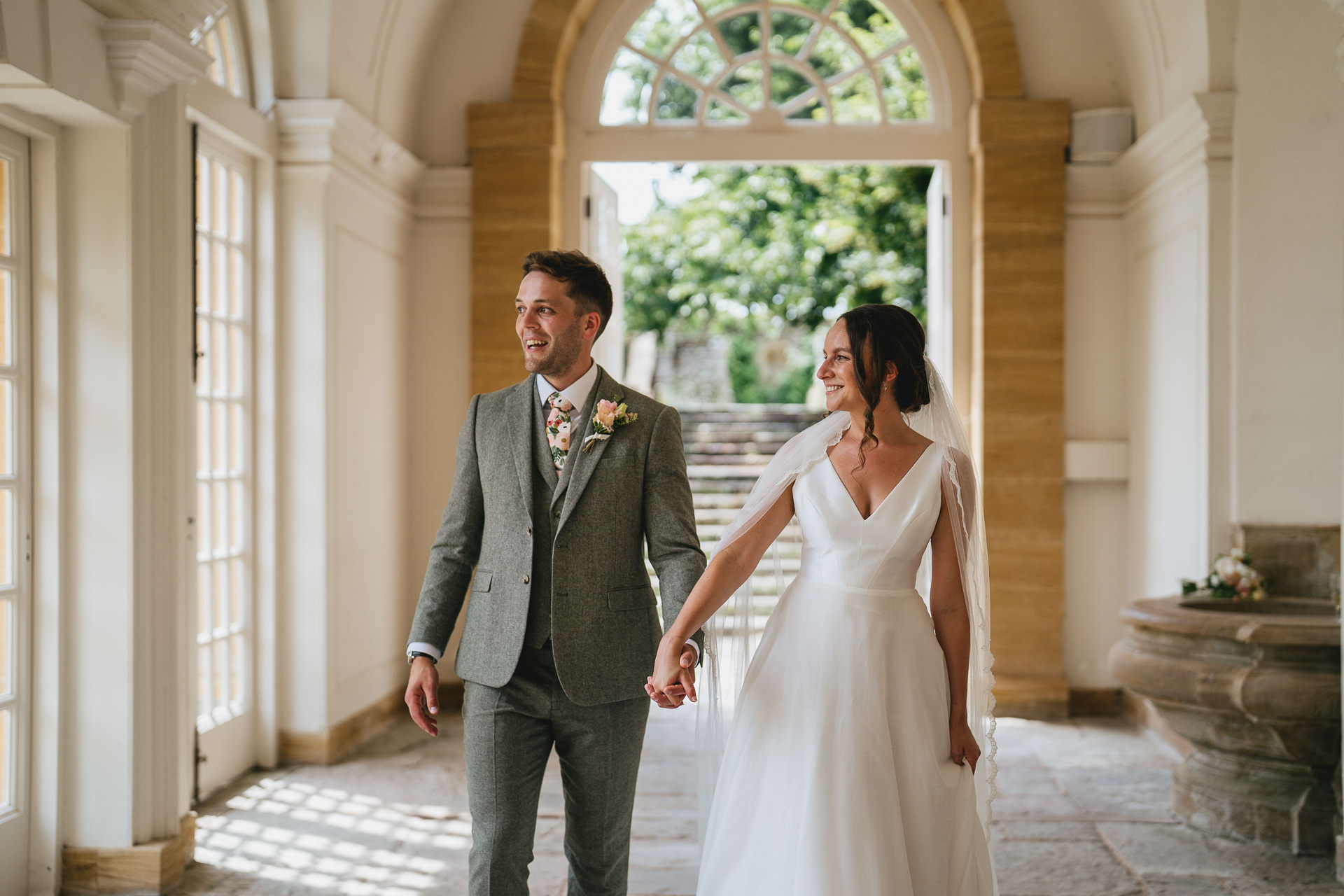 A bride and groom walking together smiling through the orangery at Hestercombe