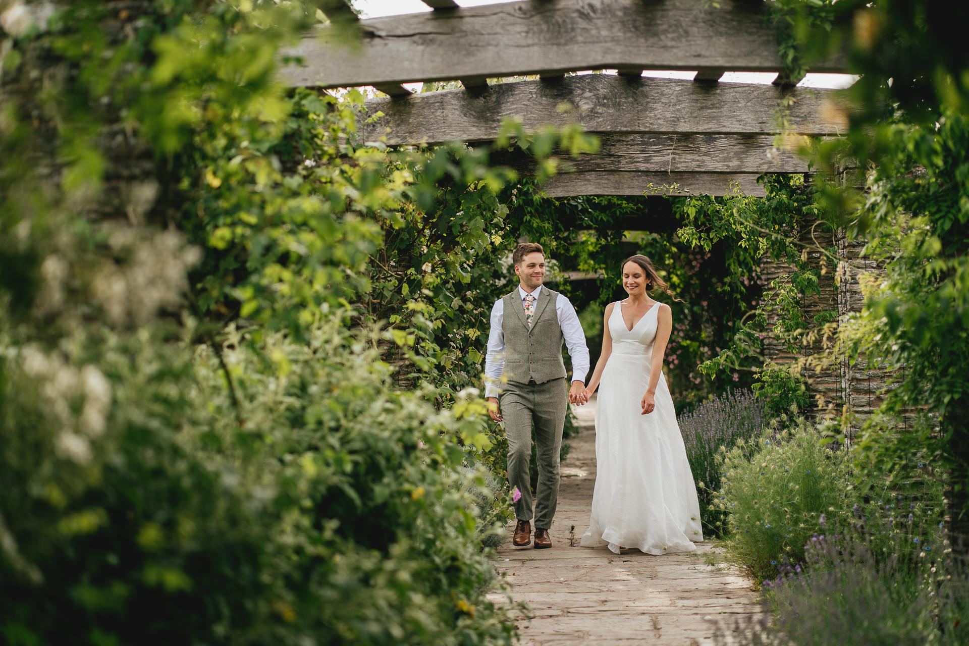 A bride and groom walking through Hestercombe Gardens smiling and talking together