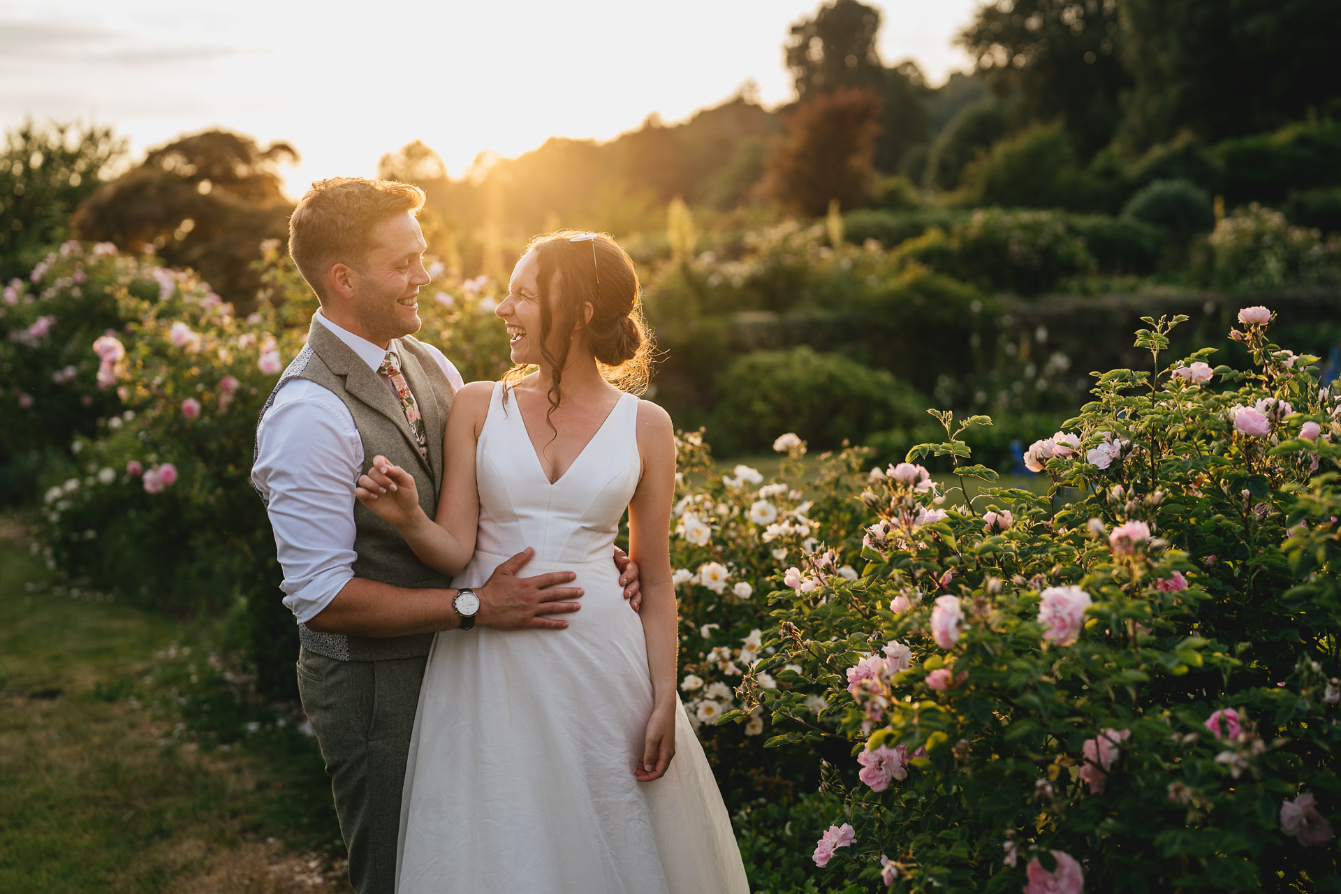 A couple in beautiful evening sunlight, laughing together in Hestercombe Gardens on their wedding day