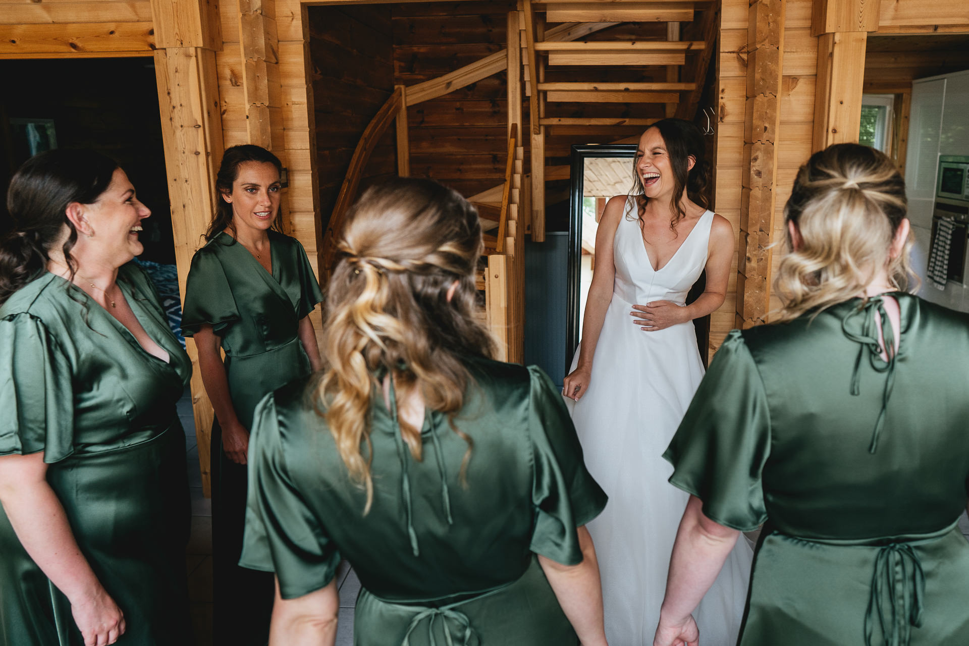 A bride laughing with a group of bridesmaids in dark green dresses