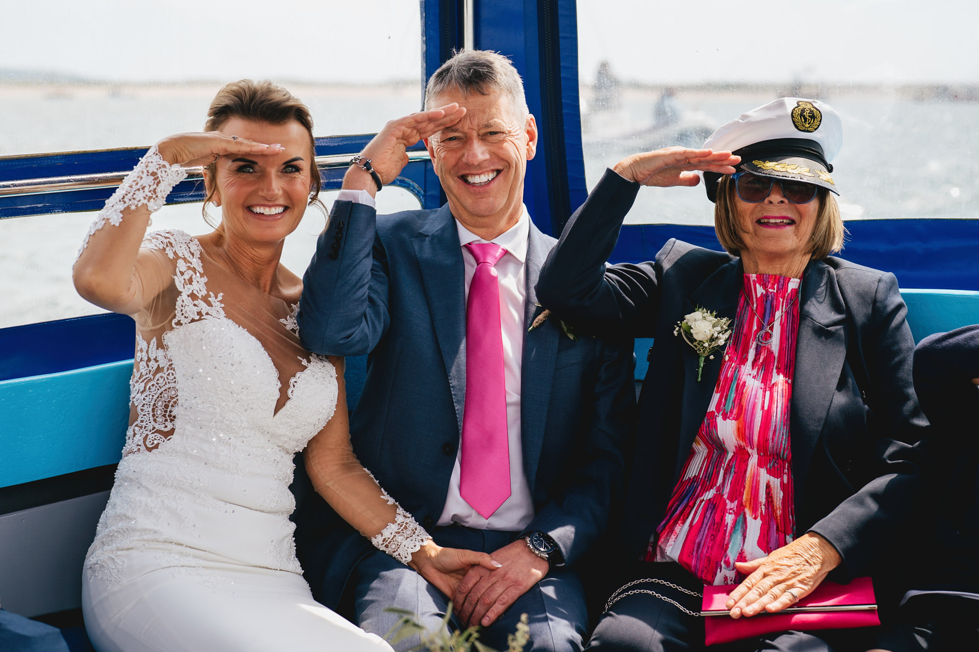 A bride and groom and mother on a boat to the River Exe Cafe giving a captain's salute to the camera