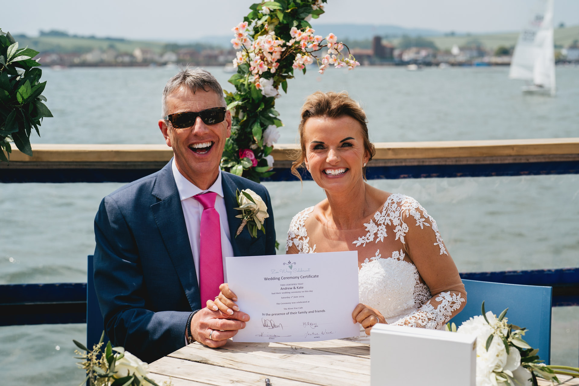 A bride and groom smiling and holding their wedding certificate on board the River Exe Cafe