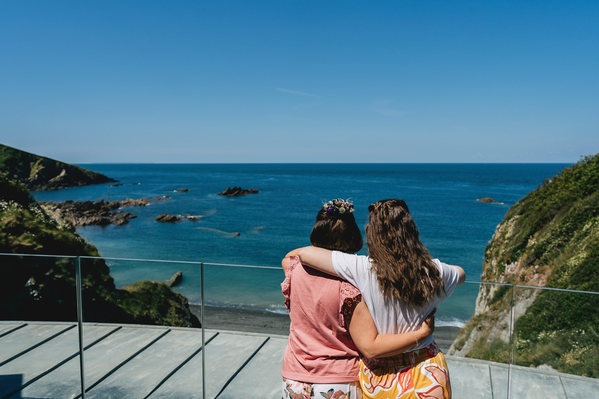 Two women with their arms around each other looking at a blue sea