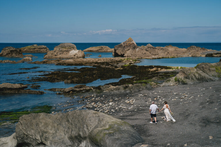 A bride and groom walking across the sand at their Tunnels Beaches elopement wedding