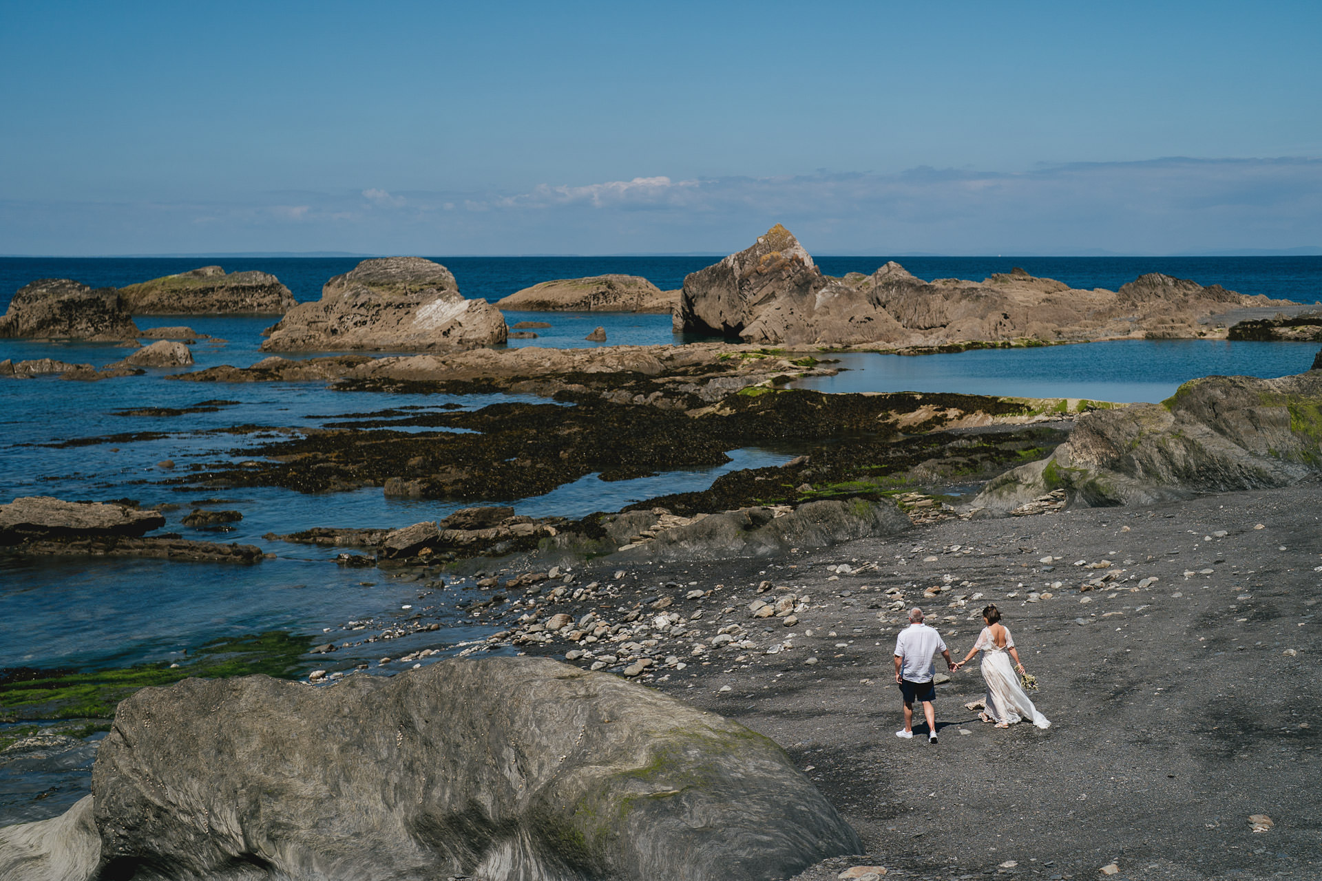 A bride and groom walking across the sand at their Tunnels Beaches elopement wedding