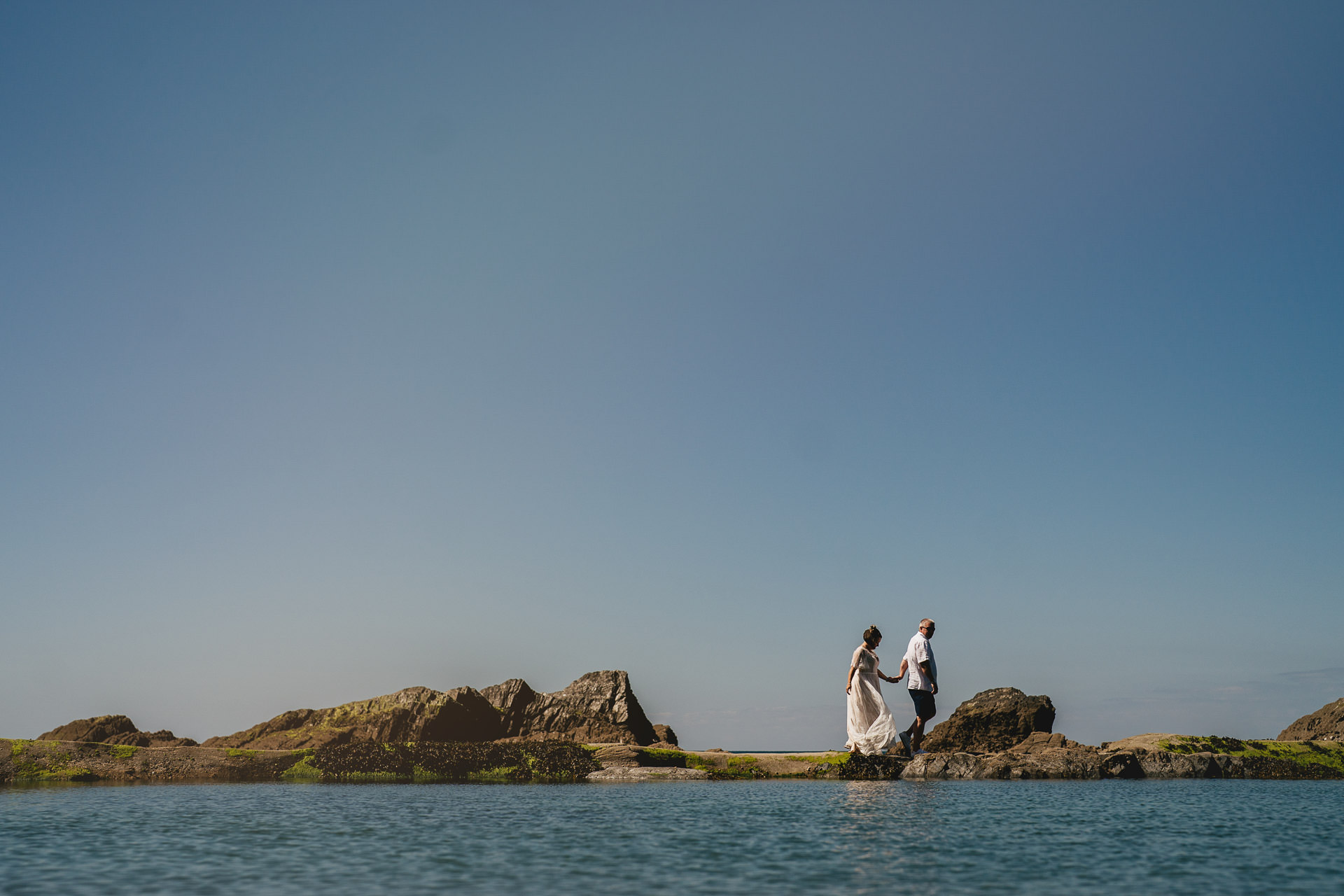 A bride and groom walking along the edge of the tidal pool at Tunnels Beaches