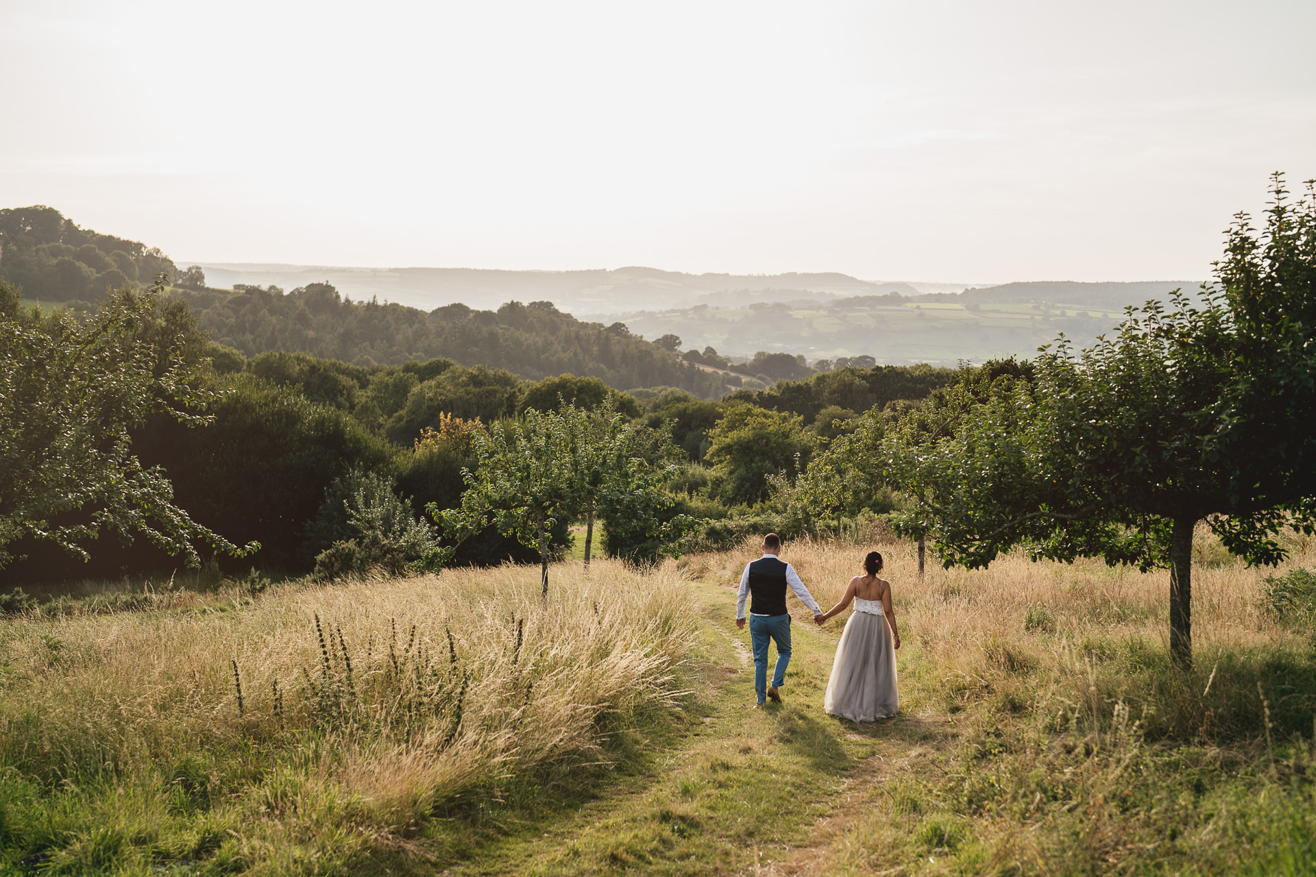 A bride and groom walking hand in hand across a field at River Cottage after their elopement wedding.