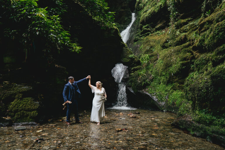 A bride and groom dancing in the water, in front of St Nectan's waterfall at their elopement wedding