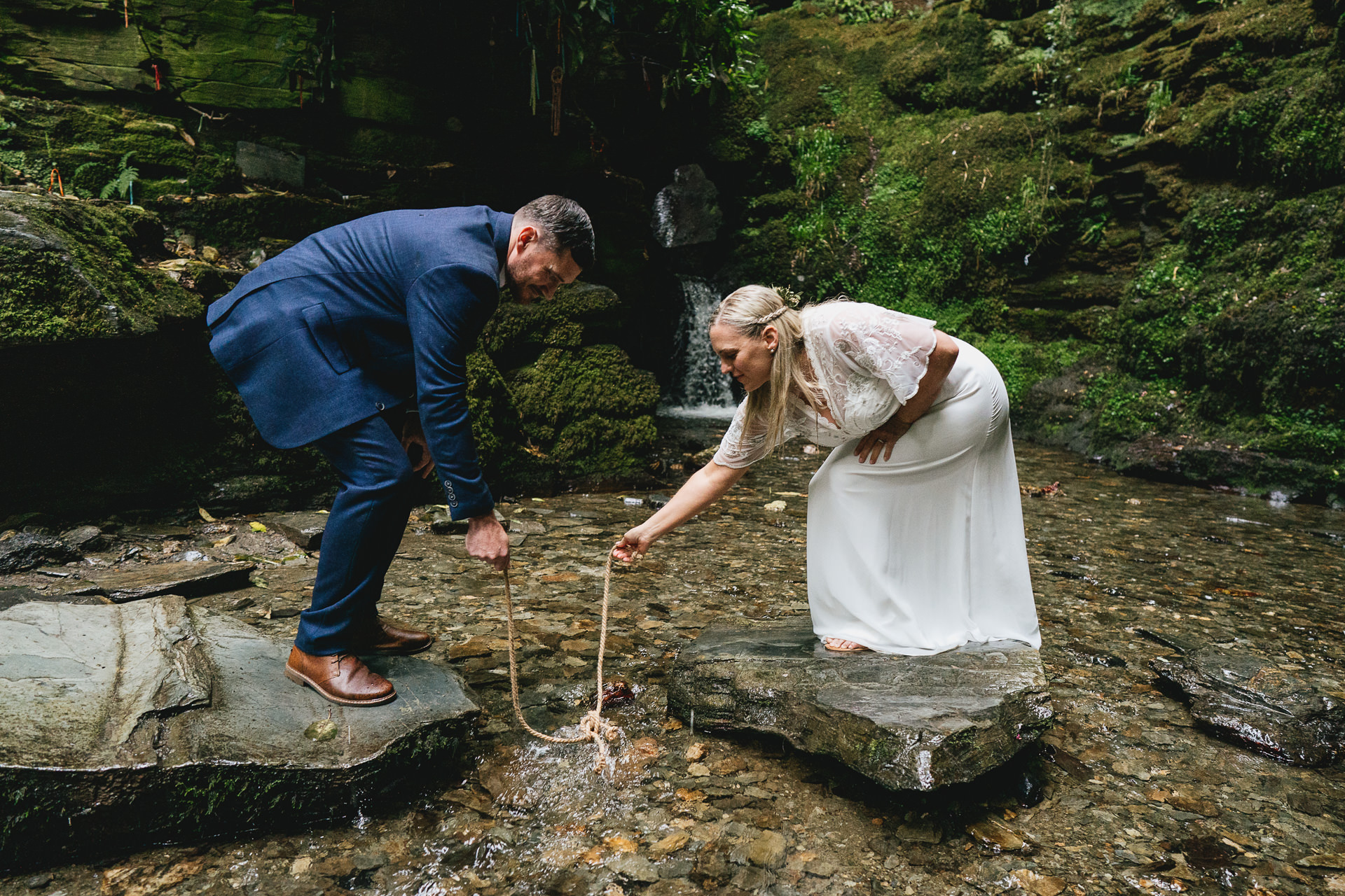 A bride and groom dipping their tied knot in the waters of St Nectan's waterfall