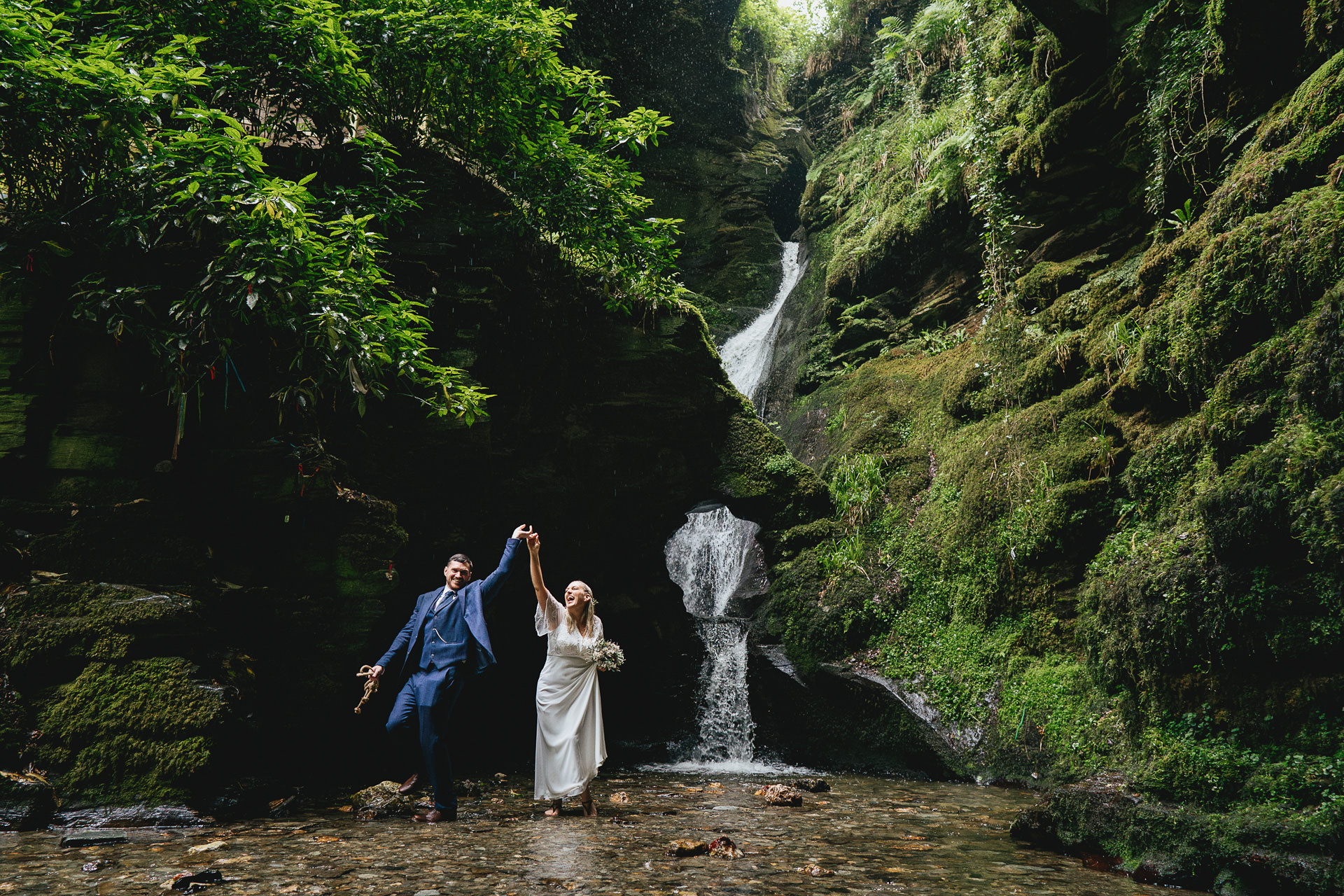 A bride and groom dancing alone in the water at St Nectan's Glen and laughing