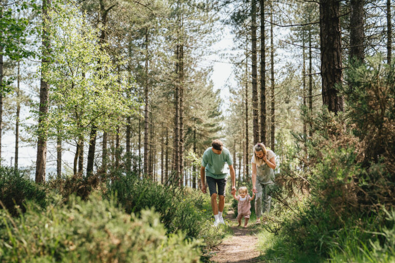 Parents walking through the trees with their toddler during the best family photography session at Woodbury Common in Devon