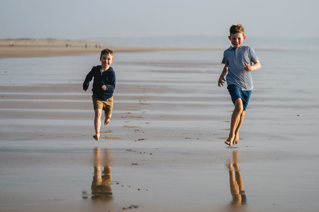 Two cousins during a family photography session in the South West running across a beach in North Devon