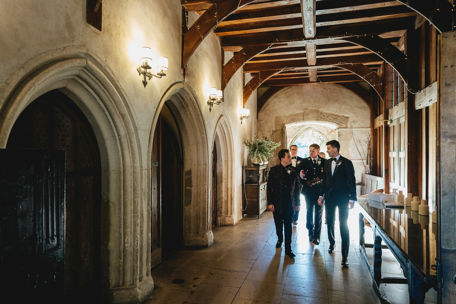 A groom and wedding party walking through a grand hallway at Dartington Hall